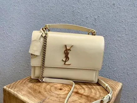 A cream flap bag with a gold chain strap, standing on a wooden block